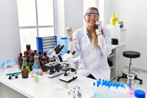 Kaunis nainen työskentelee tiedemies laboratoriossa puhuminen puhelimessa huutaa ylpeä, juhlii voittoa ja menestystä hyvin innoissaan nosti aseita  - Valokuva, kuva