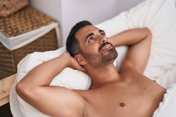 jonge latino man glimlachen zelfverzekerd liggend op bed in de slaapkamer - Foto, afbeelding