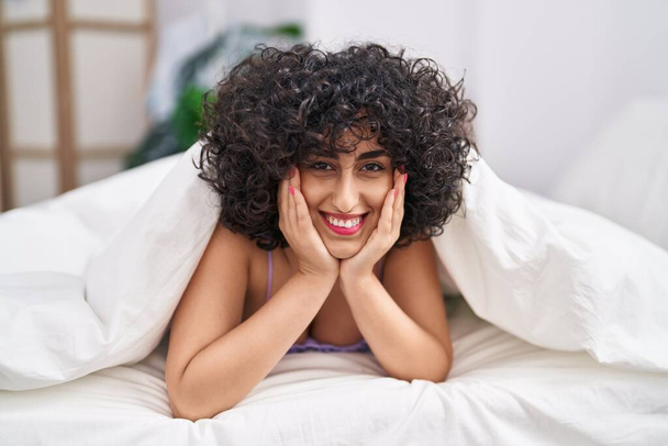 Joven mujer de Oriente Medio sonriendo confiado acostado en la cama en el dormitorio - Foto, imagen