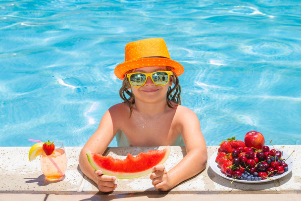 Kind eet watermeloen. Hij eet zomervruchten op het zwembad. Kind in het zwembad spelen in het zomerwater. Vakantie en reizen met kinderen - Foto, afbeelding
