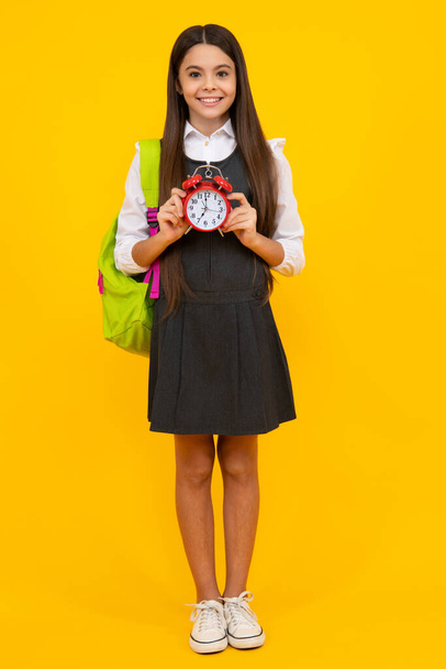 Zurück zur Schule. Teenager schulmädchen mit tasche halten wecker, zeit zum lernen. Schulmädchen auf gelbem Hintergrund. Glückliches Mädchengesicht, positive und lächelnde Emotionen - Foto, Bild