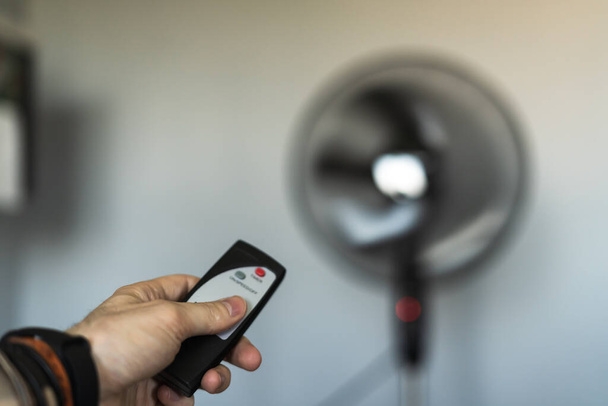 Person turning on a fan in the middle of a heat wave with a remote control - 写真・画像