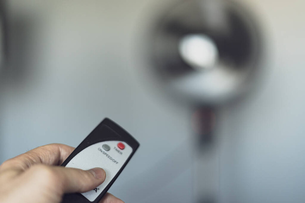 Person turning on a fan in the middle of a heat wave with a remote control - Photo, Image
