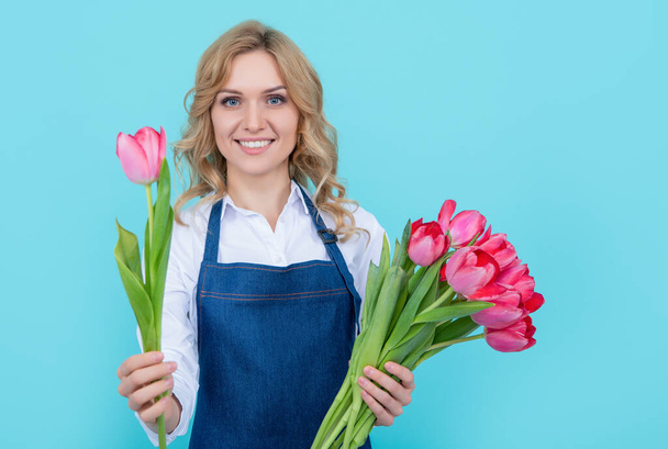 glad girl in apron with spring tulip flowers on blue background. - Foto, imagen