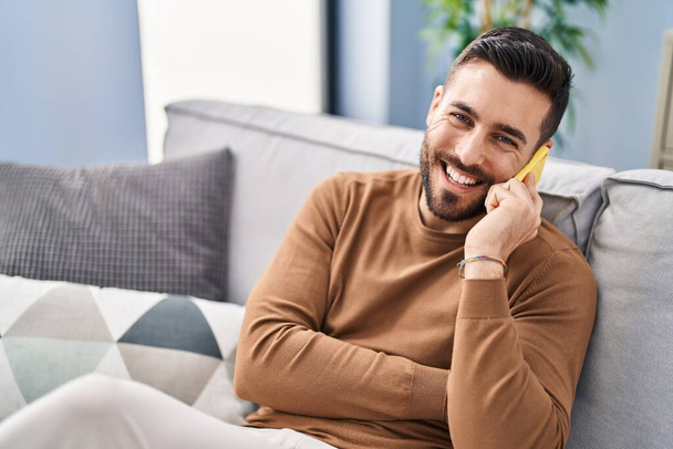 Young hispanic man talking on the smartphone sitting on sofa at home - Photo, image