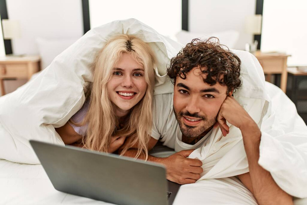 молода пара лежить на ліжку з ноутбуком і посміхається
 - Фото, зображення