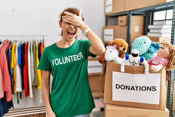 Beautiful caucasian woman wearing volunteer t shirt at donations stand smiling and laughing with hand on face covering eyes for surprise. blind concept.  - Foto, immagini