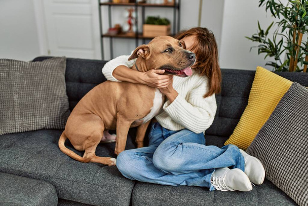 Junge kaukasische Frau küsst und umarmt Hund, der zu Hause auf Sofa sitzt - Foto, Bild