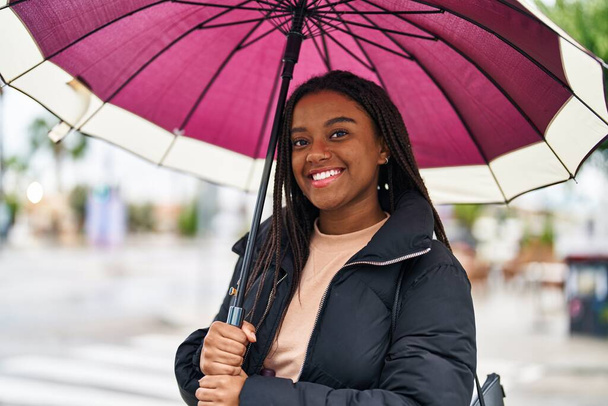 afro-américaine femme souriant confiant en utilisant parapluie à la rue - Photo, image
