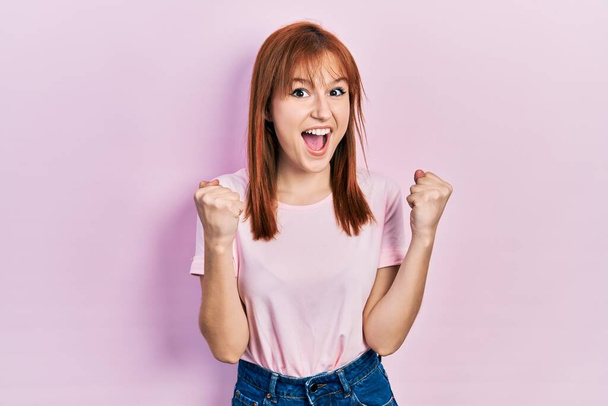Rossa giovane donna indossa casual t shirt rosa che celebra sorpreso e stupito per il successo con le braccia alzate e occhi aperti. concetto di vincitore.  - Foto, immagini