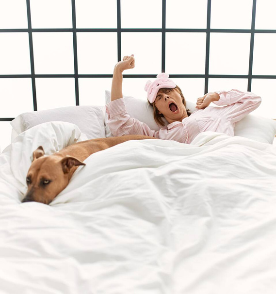 Young caucasian woman waking up lying on bed with dog at bedroom - Foto, immagini