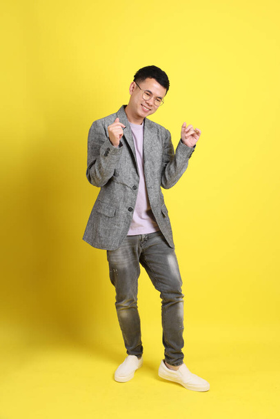 The Asian LGBTQ man with grey blazer standing on the yellow background. - Фото, изображение