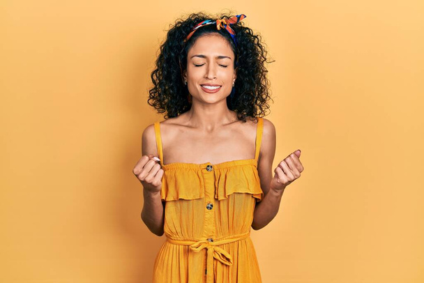 Fiatal latin lány visel nyári ruha izgatott a siker karját, és csukott szemmel ünneplő győzelem mosolyogva. győztes koncepció.  - Fotó, kép
