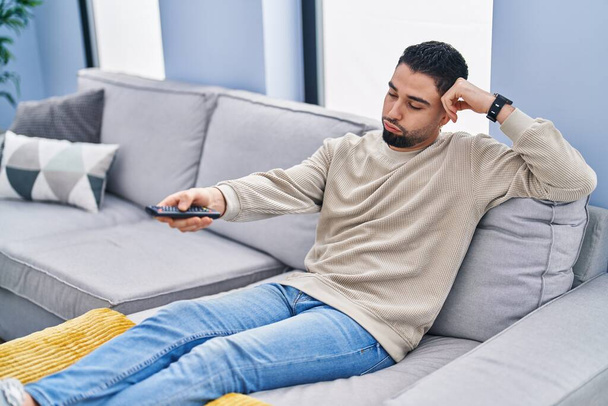 Young arab man watching tv with boring expression at home - Foto, Imagem