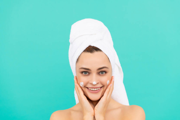 cheerful young lady applying face cream on blue background. - Foto, imagen