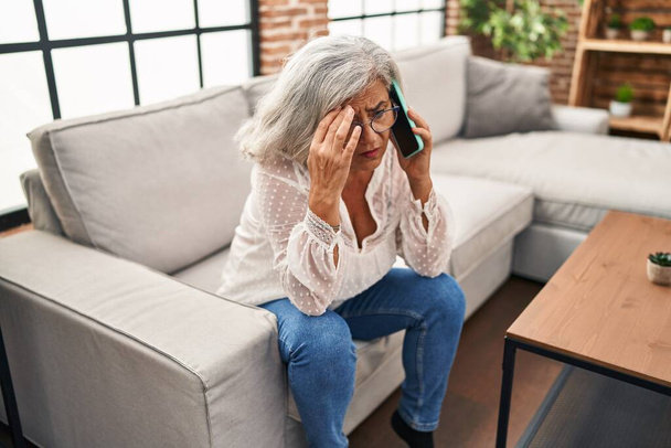 Женщина средних лет беспокоилась, разговаривая по смартфону дома - Фото, изображение