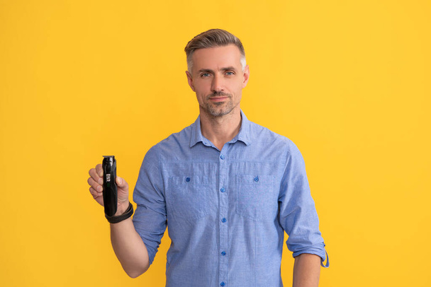 man hold electric razor on yellow background, shaving. - Photo, Image