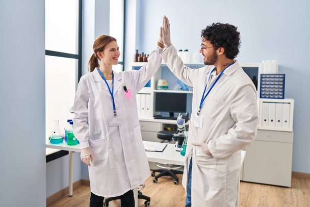 Man and woman scientist partners high five with hands raised up at laboratory - Φωτογραφία, εικόνα