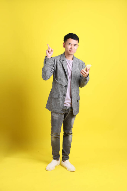 The Asian LGBTQ man with grey blazer standing on the yellow background. - Zdjęcie, obraz