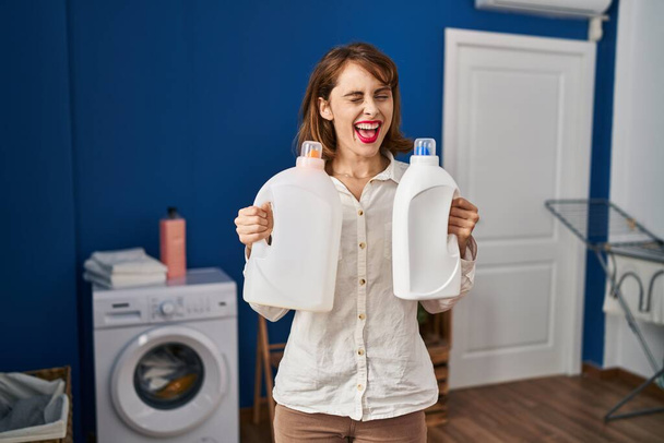 Young beautiful woman holding detergent bottles winking looking at the camera with sexy expression, cheerful and happy face.  - Foto, Bild