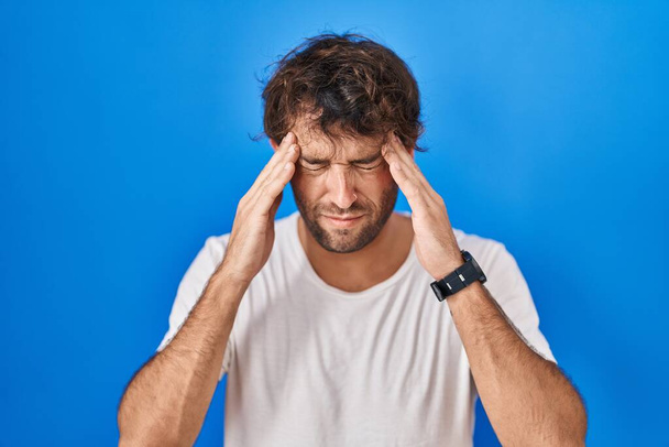 Spanyol fiatalember, kék háttér fölött áll, fejfájással, mert stresszes. migrénben szenved.  - Fotó, kép