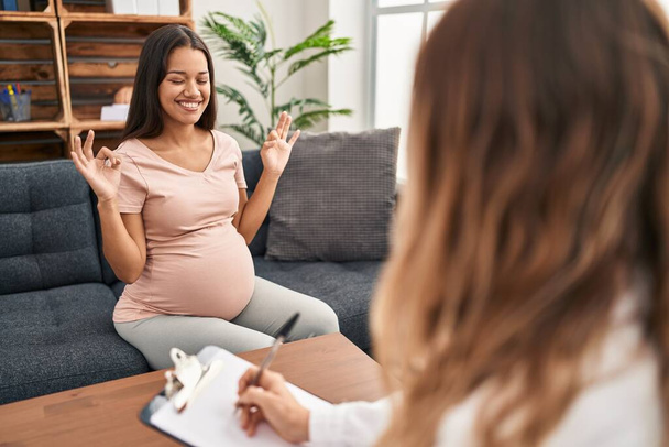 Young pregnant woman at therapy session relax and smiling with eyes closed doing meditation gesture with fingers. yoga concept.  - Zdjęcie, obraz