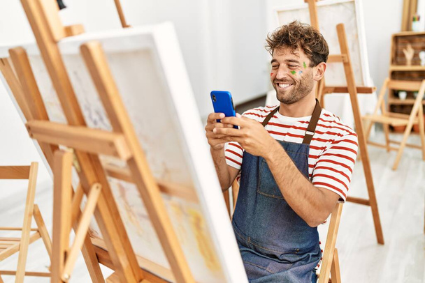Young hispanic man make photo to draw using smartphone at art studio - Photo, image