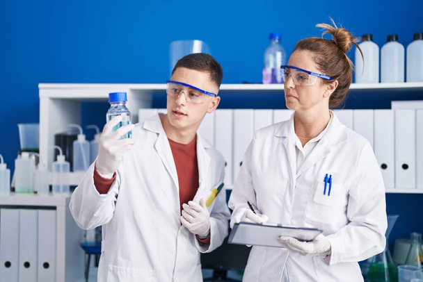 Man and woman scientists write on document holding bottle at laboratory - Foto, immagini