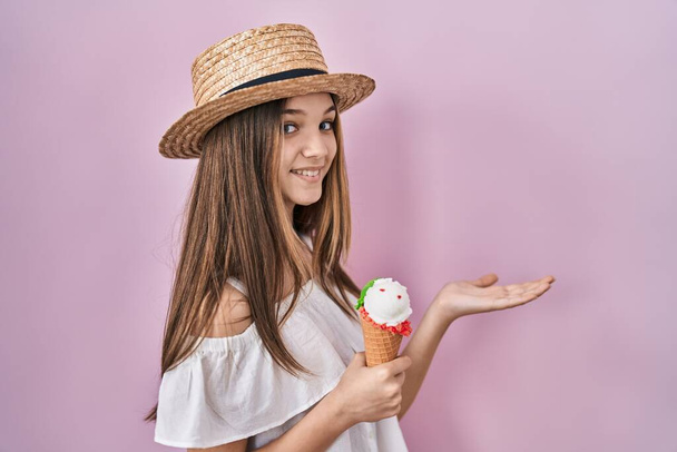 Teenager dívka drží zmrzlinu ukazuje stranou s rukama otevřenýma dlaněmi ukazující kopírovací prostor, prezentuje reklamu s nadšeným úsměvem  - Fotografie, Obrázek