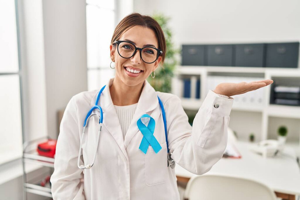 Young brunette doctor woman wearing stethoscope at the clinic smiling cheerful presenting and pointing with palm of hand looking at the camera.  - Φωτογραφία, εικόνα