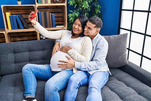 Młoda Latynoska para spodziewa się selfie dziecka przez smartfona w domu - Zdjęcie, obraz