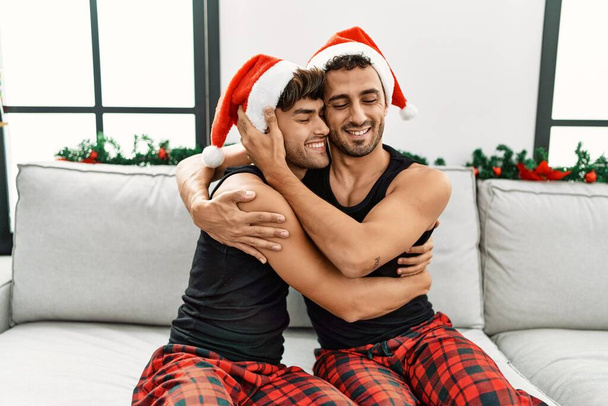 Dwóch Hiszpanów przytula się do siebie siedząc przed świątecznym wystrojem w domu. - Zdjęcie, obraz