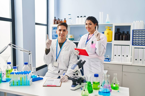 Fiatal orvosok dolgoznak a tudós laboratóriumban mosolyogva egy ötlettel vagy kérdéssel ujjal mutogatva boldog arccal, első számú  - Fotó, kép