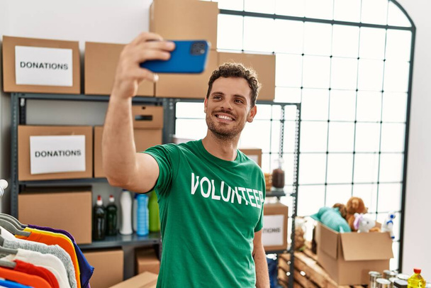 Giovane uomo ispanico indossando uniforme volontaria fare selfie dallo smartphone al centro di beneficenza - Foto, immagini