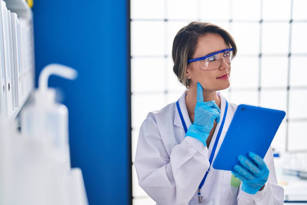 Young woman scientist using touchpad with doubt expression at laboratory - Foto, Bild