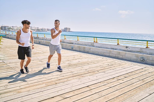 İki İspanyol erkek, sportif, gülümseyen bir çift, deniz kenarında koşuyorlar. - Fotoğraf, Görsel