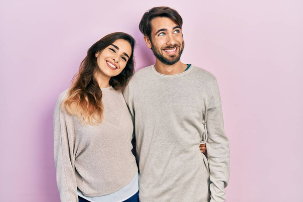 Mladý hispánský pár nosí ležérní oblečení, usmívá se a dívá se stranou a přemýšlí.  - Fotografie, Obrázek