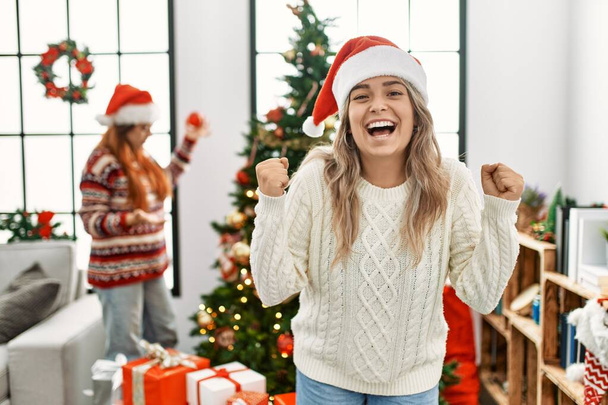 Красивая пара дома, стоящая у рождественской елки, гордо крича, празднуя победу и успех, очень взволнована поднятыми руками  - Фото, изображение