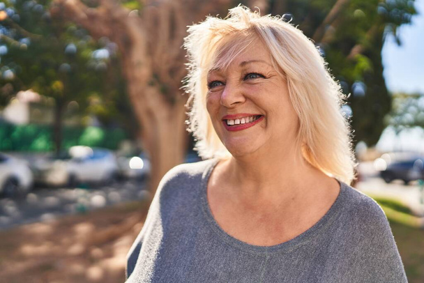 Blonde Frau mittleren Alters lächelt selbstbewusst im Park - Foto, Bild