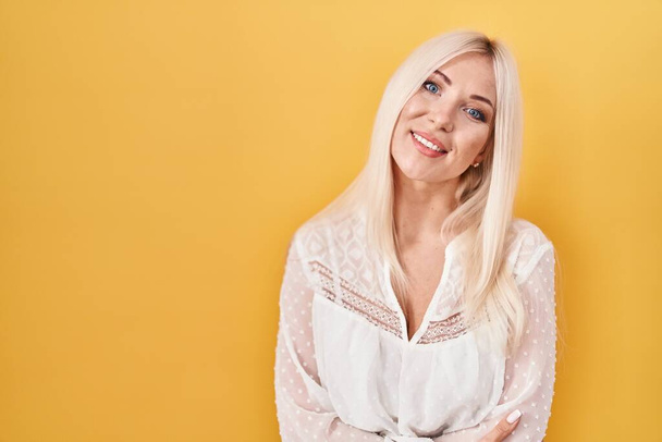 Caucasian woman standing over yellow background happy face smiling with crossed arms looking at the camera. positive person.  - Fotoğraf, Görsel
