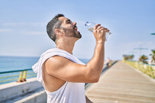 Hispanic sports man wearing workout style drinking water to stay hydrated outdoors on a sunny day - Photo, Image