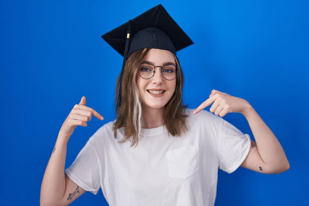 Mujer rubia caucásica con gorra de graduación mirando confiado con sonrisa en la cara, señalándose con los dedos orgullosos y felices.  - Foto, imagen