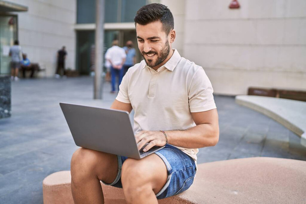 Jovem hispânico sorrindo confiante usando laptop na rua - Foto, Imagem