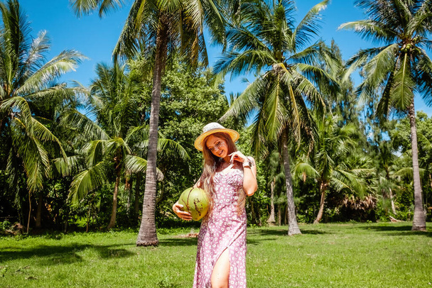 Summer holidays, vacation concept. Smiling travel women holding young green coconut among exotic tropical palm trees. Beautiful girl under branches of the palm trees, relaxing on travel vacation. - Photo, Image