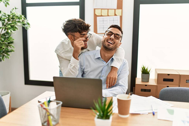 Two hispanic men couple hugging each other working at office - 写真・画像