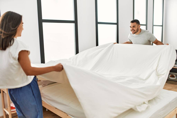 Jeune couple latino souriant heureux de faire leur lit à la maison. - Photo, image