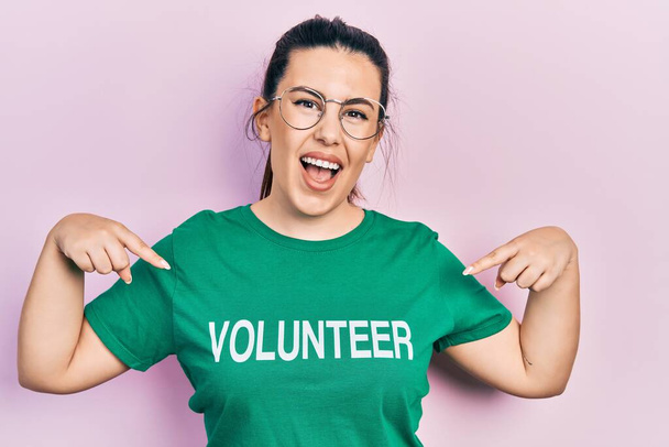 Young hispanic woman wearing volunteer t shirt looking confident with smile on face, pointing oneself with fingers proud and happy.  - Foto, imagen