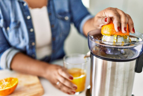 Hispanic brunette woman preparing orange juice at the kitchen - Photo, Image