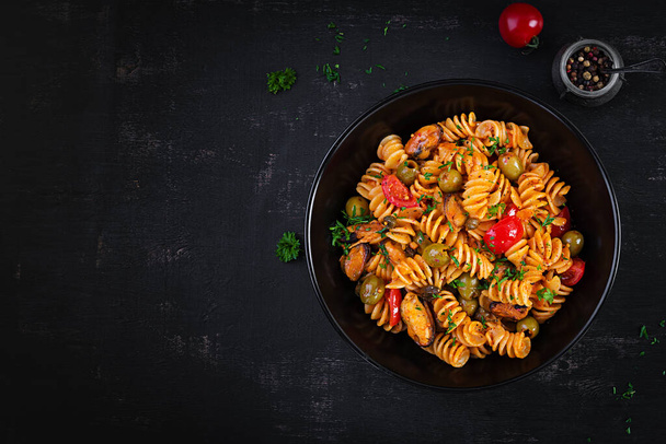 Klassinen italialainen pasta fusilli marinara simpukoilla, vihreillä oliiveilla ja kaprikoilla pimeällä pöydällä. Fusilli-pastaa kastikkeella marinara. Ylhäältä katsottuna - Valokuva, kuva