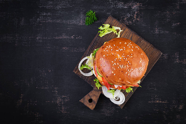 Hamburger with chicken burger meat, cheese, tomato, cucumber and lettuce on wooden background. Tasty burger. Close up. Top view - 写真・画像